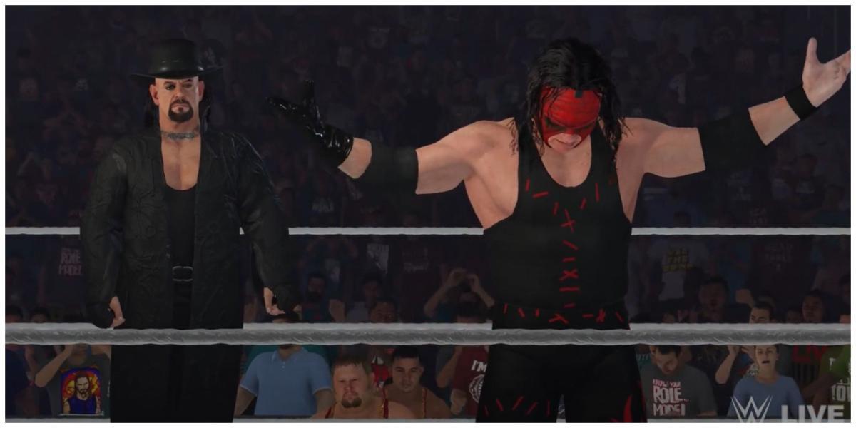 The Undertaker e Kane no ringue em WWE 2K23. Undertaker está vestindo um casaco preto e chapéu de aba, Kane está com uma máscara vermelha e está levantando os braços no ar.