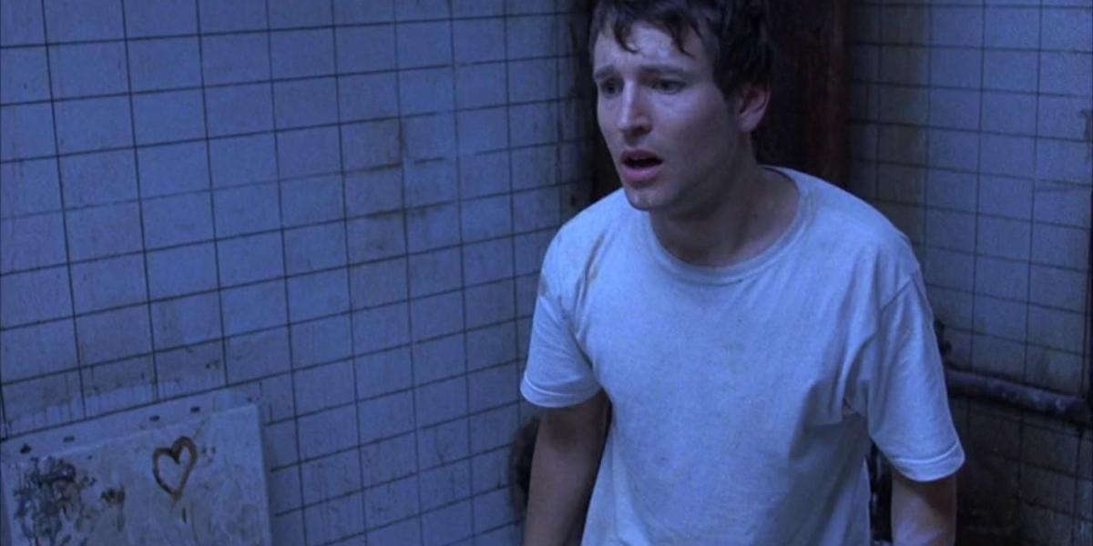 Leigh Whannell como Adam parecendo assustado em Jogos Mortais (2004)