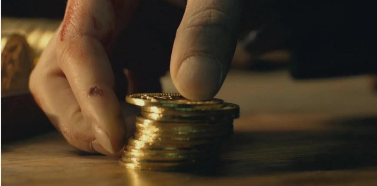 Mão segurando uma pilha de moedas de ouro (John Wick)