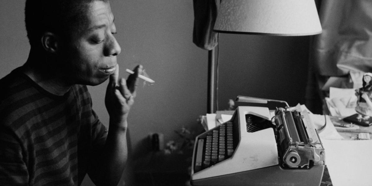 (Foto) foto em preto e branco de um homem negro fumando um cigarro na frente de uma máquina de escrever