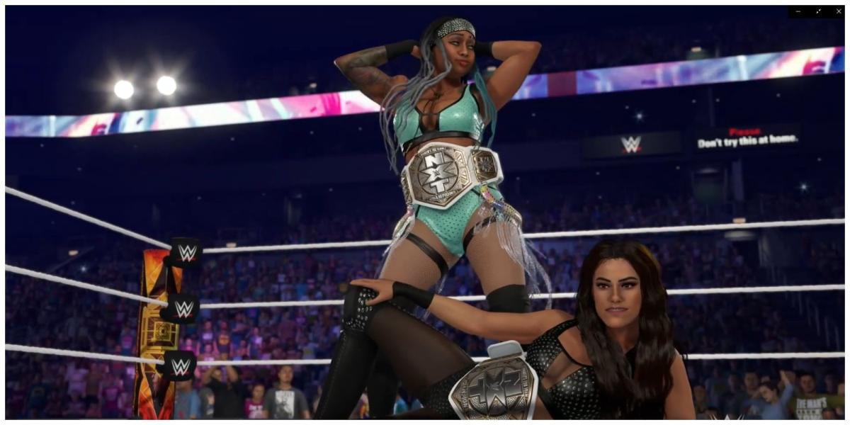 Katana Chance em pé atrás de Kayden Carter balançando os quadris. Carter está deitado, ambas as mulheres estão no ringue da WWE usando o NXT Women's Championships