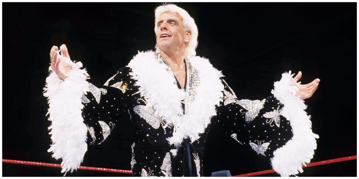 Ric Flair em um ringue da WWE vestindo uma túnica preta com penas brancas segurando os braços para fora