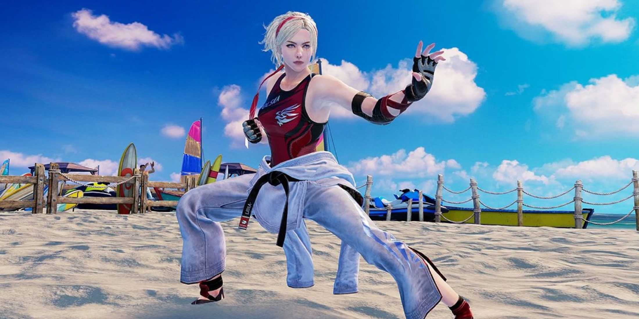 Lidia Sobieska from Tekken 7 strikes a martial arts pose on a sandy beach, wearing a red and black top