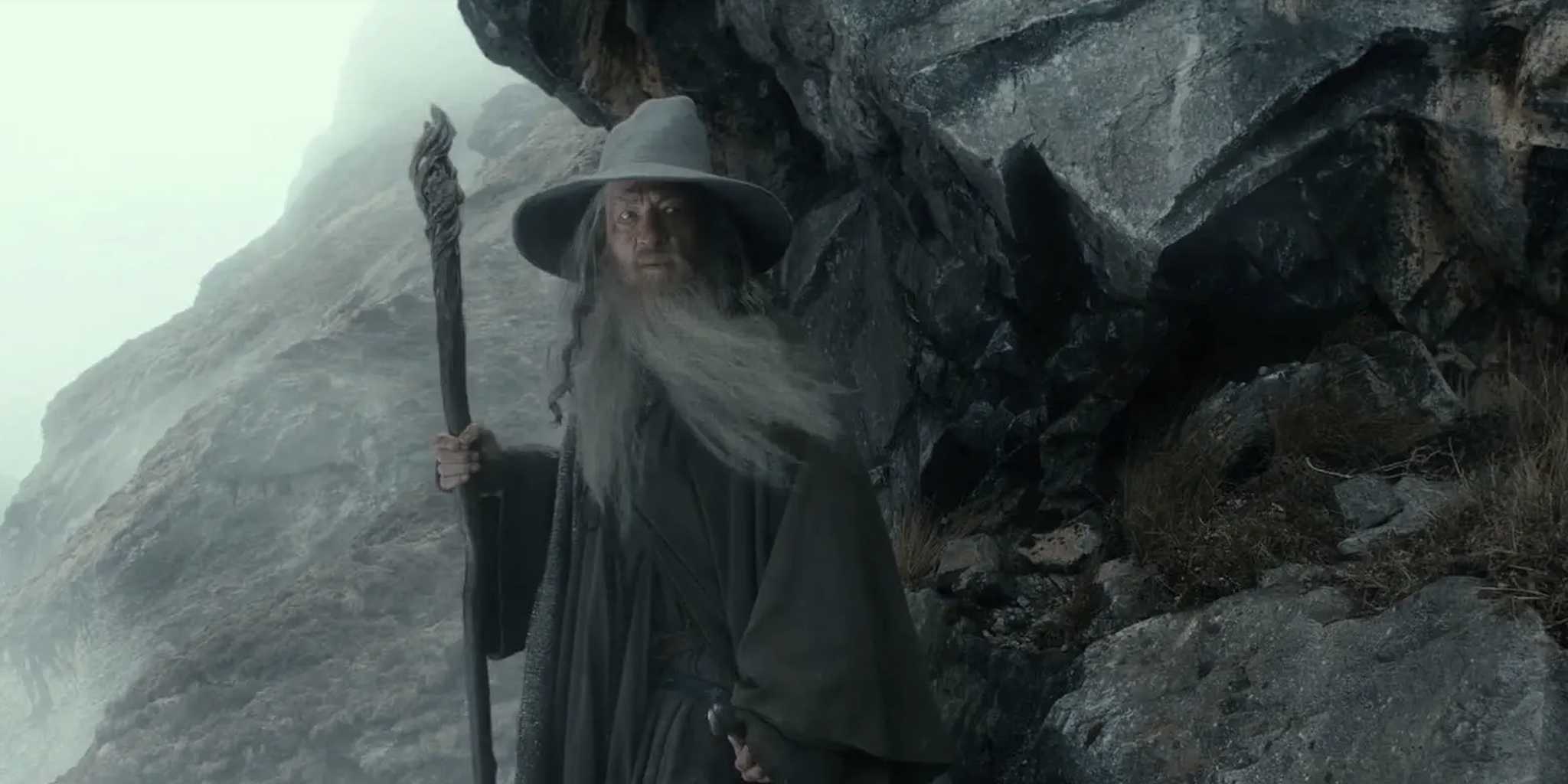 Gandalf standing against a rocky cliff face in the Hobbit/LOTR